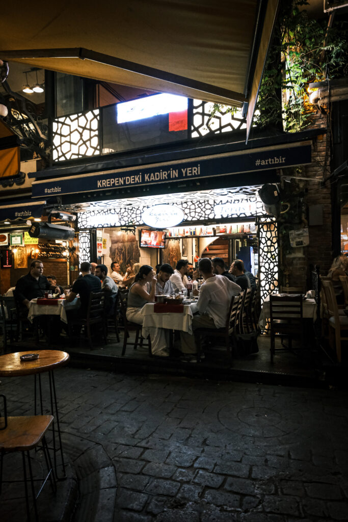 Loş ışıkta çekilmiş, üzerinde rakı kadehi, topik ve lakerda mezeleri bulunan, rezerve edilmiş tarihi Gedikli İstanbul Meyhaneleri masası.